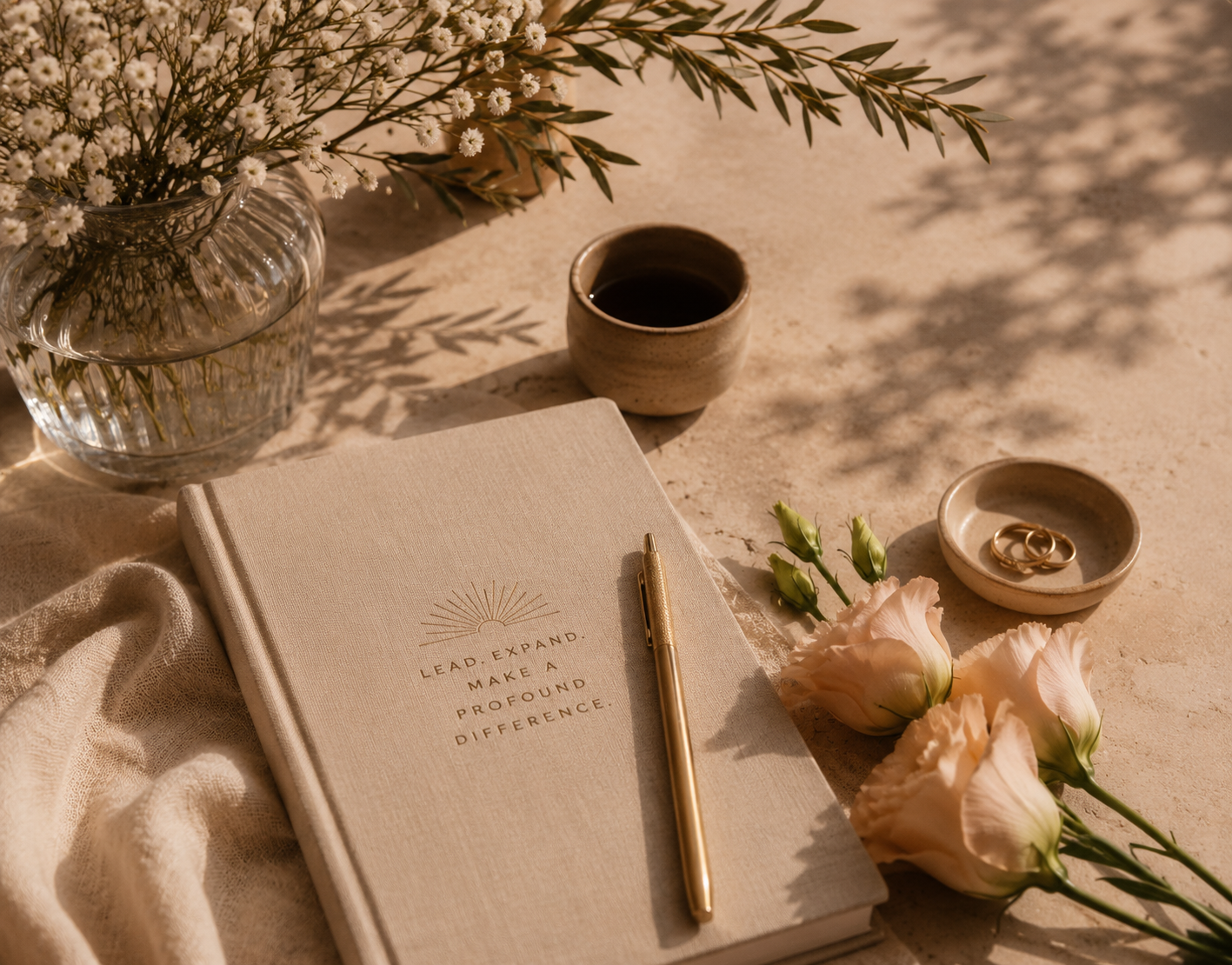 Linen journal with gold pen, flowers and coffee in warm sunlight